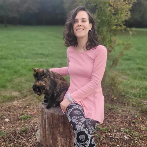 Gabrielle Vatin — jeune femme souriante aux cheveux bouclés, assise sur une souche avec un chat