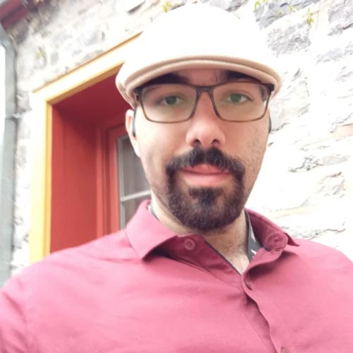 Jérémie — un homme avec une barbe, des lunettes et une casquette beige devant un mur en pierre