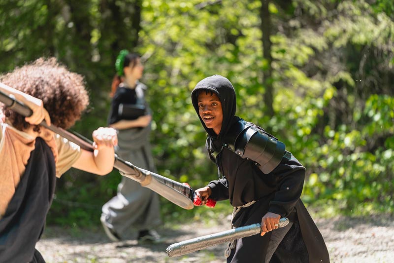 Jeunes en costumes médiévaux s'affrontant à l'épée de mousse en forêt