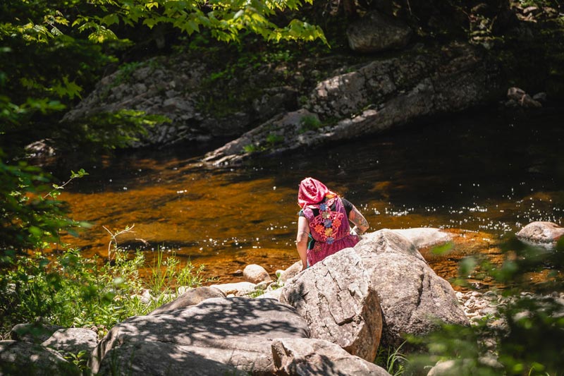 Personnage en costume médiéval-fantastique méditant au bord d'une rivière en forêt